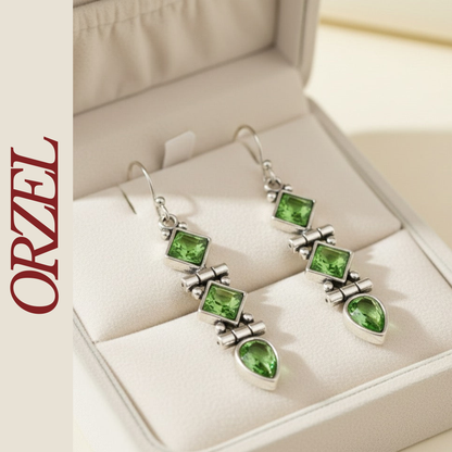 Boucles d’oreilles pendantes argentées avec pierres vertes géométriques.